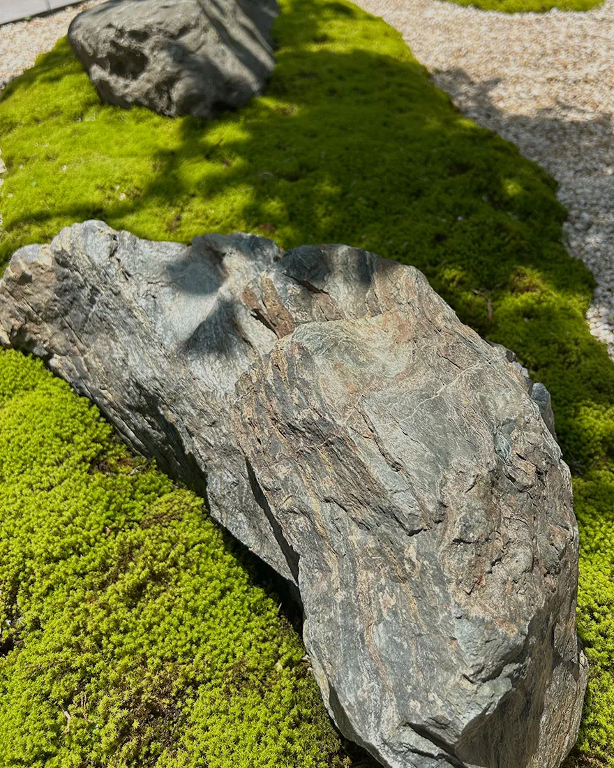 鮮やかな緑の苔の上に配置された、味わいのある大きな景石