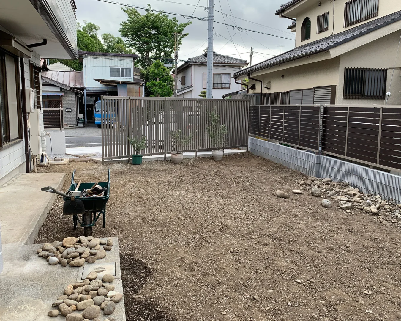 庭づくりの着工前の様子。一輪車や道具、石が置かれた、広く平らな土の状態のバックヤードスペース。