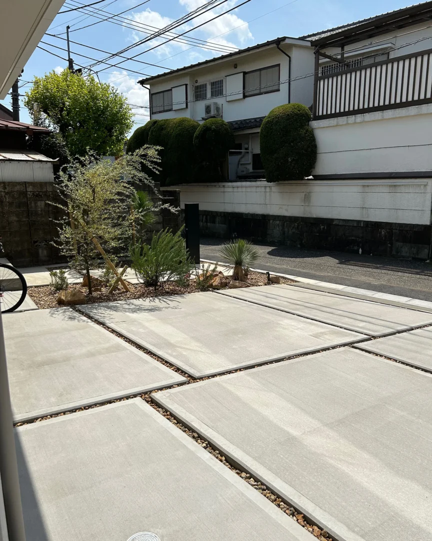 住宅側から見下ろした、美しいスリットと砂利敷きが目を引く広々としたコンクリートの駐車スペースと左手の植栽帯。