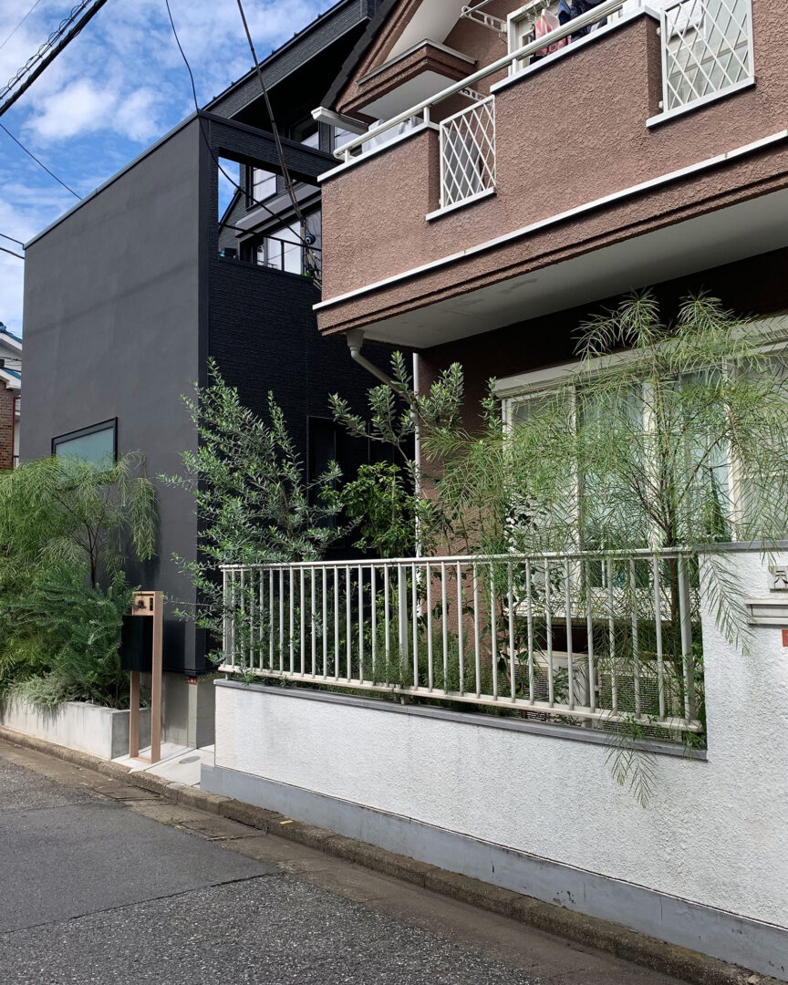 ご実家の白い塀と手すりの一部を加工し、新築の黒い建物と行き来がしやすくなった、緑豊かなアプローチの全景。